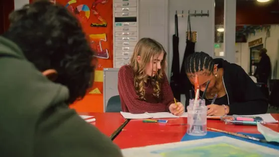 A photograph of three teenagers working at a desk.