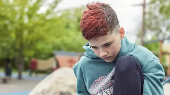 Photo of a teenager sitting outside looking down at their phone.