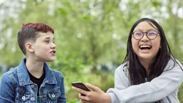 Two children outside, one using their mobile phone