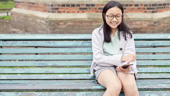 Photograph of a child sat using their mobile phone while sat on a bench outside.