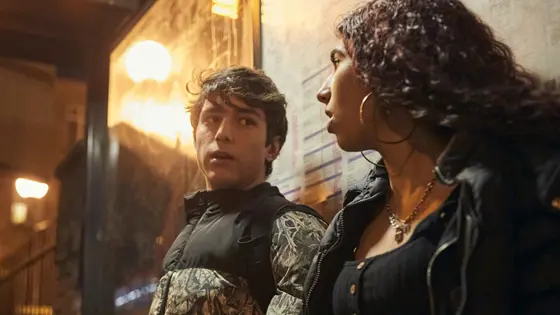 A teenage girl and a teenage boy sat at a bus stop talking to each other.