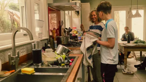 A carer smiling while washing dishes with a teenager.