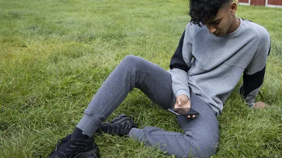 Teenage boy sat on the grass looking at his phone
