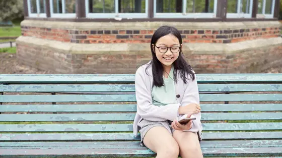 Photograph of a child sat on a bench outdoors, using their mobile phone.