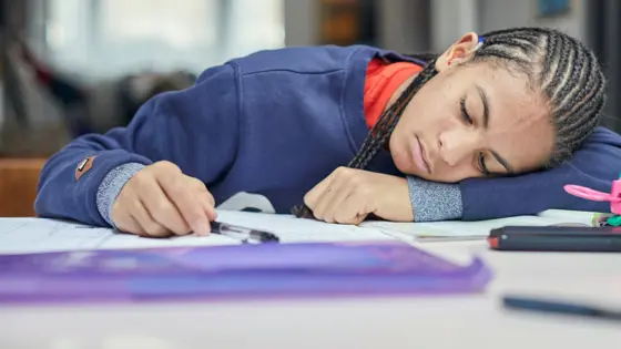 Photo of a teenager with their head on the desk looking at their work.